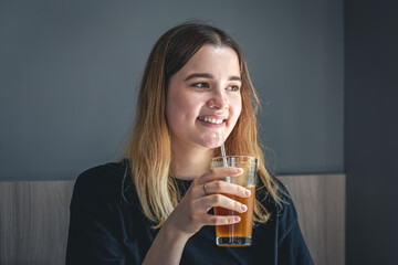 A young woman drinking cold summer coffee drink with ice and orange juice.