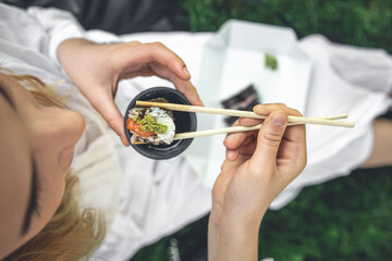 A young woman eating sushi in nature, maki roll close-up. © puhimec