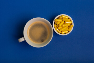 Cup of coffee and vitamins in white jar on blue background from above. Morning rituals and healthy lifestyle.