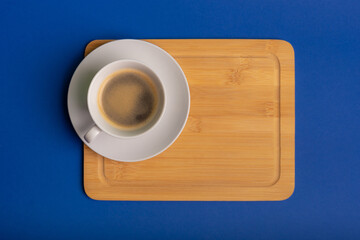 Mug of black coffee with foam on wooden desk on blue background from above. Morning rituals.