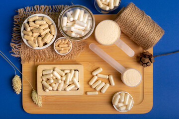 Many jars with different vitamins and minerals from above on dark blue background. Health Supplements. Lactose free and no gluten food supplements and sport food on a wooden desk on blue background.