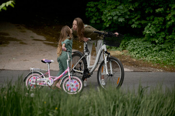 Naklejka premium Mom and daughter cycling in the park. Children summer vacation concept