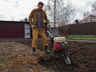 Farmer cultivates the ground soil in the garden using a motor cultivator or tiller tractor. Modern farming and technology agriculture. 