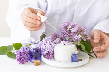 Obraz na płótnie Canvas Female scientist doing laboratory research with natural organic essential oils and flower extracts. Lilac for anti-age and anti-acne therapy, moisturizing. White background.