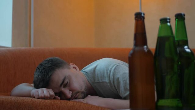 Young sleepy man waking up in bed after alcohol abuse and drug addiction looking at the bottles with alcohol. Male laying in the bed after party looking around and remembering last night's events
