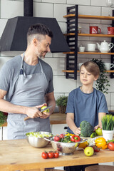 Handsome father and his teenager son spending quality time together. Men doing chores, cooking healthy vegetable salad, tasty food in the kitchen at home