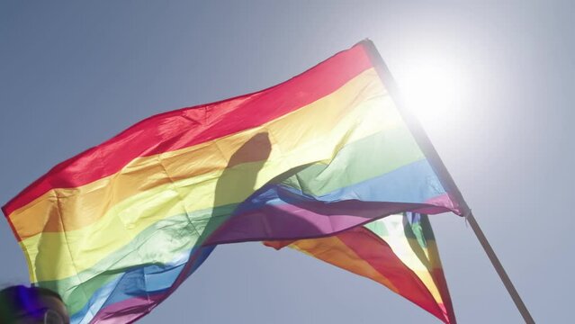 LGBTQ rainbow flag waving in slow motion during the main party in a pride parade with thousands of people