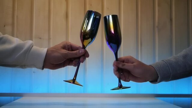 Close up of two male hands clinking fancy glasses and toasting. Concept of two gay men on a date drinking alcohol from champagne glasses. Pair of masculine hands cheering with thin colorful glasses