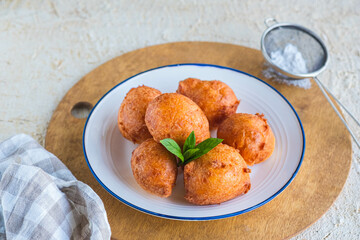Deep fried round donuts on a white plate on a light concrete background. Deep-fried baking.