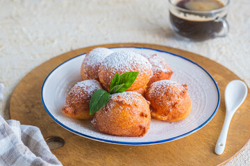 Deep fried round donuts on a white plate on a light concrete background. Deep-fried baking.