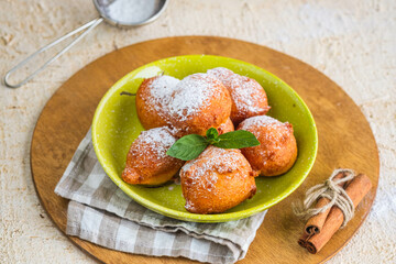 Deep fried round donuts on a green plate on a light concrete background. Deep-fried baking