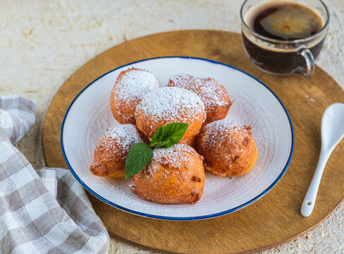 Deep fried round donuts on a white plate on a light concrete background. Deep-fried baking.