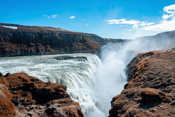 Powerful cascades of Gullfoss waterfall in Golden Circle. Beautiful fog of falling water amidst rock formation against blue sky. Idyllic natural scenery in valley.