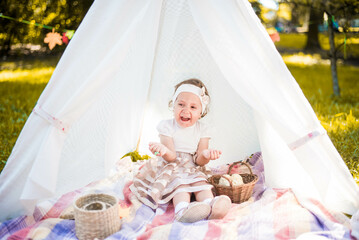 Little girl lying and playing in a tent, children's house wigwam in park Autumn portrait of cute curly girl. Harvest or Thanksgiving. autumn decor, party, picnic. Child in white dress with pumpkins.  © MartaKlos