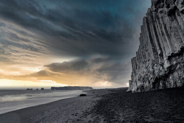 Scenic lightning over seascape at Reynisfjara Beach. Footprints on black sand seashore against...