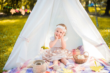 Fototapeta na wymiar Little girl lying and playing in a tent, children's house wigwam in park Autumn portrait of cute curly girl. Harvest or Thanksgiving. autumn decor, party, picnic. Child in white dress with pumpkins. 