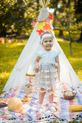 Little girl lying and playing in a tent, children's house wigwam in park Autumn portrait of cute curly girl. Harvest or Thanksgiving. autumn decor, party, picnic. Child in white dress with pumpkins.  © MartaKlos