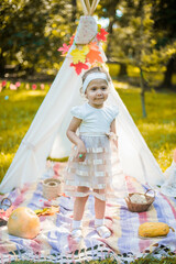 Little girl lying and playing in a tent, children's house wigwam in park Autumn portrait of cute curly girl. Harvest or Thanksgiving. autumn decor, party, picnic. Child in white dress with pumpkins.  © MartaKlos