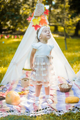 Little girl lying and playing in a tent, children's house wigwam in park Autumn portrait of cute curly girl. Harvest or Thanksgiving. autumn decor, party, picnic. Child in white dress with pumpkins.  © MartaKlos