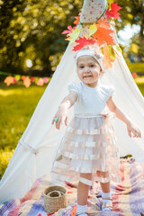 Little girl lying and playing in a tent, children's house wigwam in park Autumn portrait of cute curly girl. Harvest or Thanksgiving. autumn decor, party, picnic. Child in white dress with pumpkins.  © MartaKlos