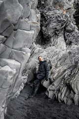 Thoughtful tourist standing against beautiful basalt columns. Man looking away while exploring rocky formation on seashore. Idyllic view of gray patterned stones at famous Reynisfjara Beach.