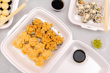 Set of fish sushi rolls with salmon and sesame,ginger,wasabi,soy sauce packed in plastic disposable container box on gray background.Seafood,Food delivery,take out service from restaurant concept