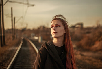 Young lonely woman walking along railway track, on background of industrial city, in dramatic and anti-utopia style