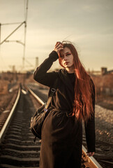 Young lonely woman walking along railway track, on background of industrial city, in dramatic and anti-utopia style