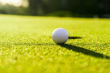 Golf ball on the green grass near hole on a golf course at sunset
