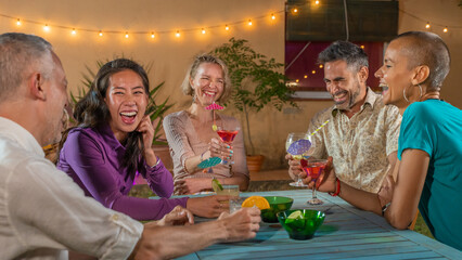 Cheerful friends drinking cocktails. Mature people having fun summer night. Lifestyle and nightlife concept.