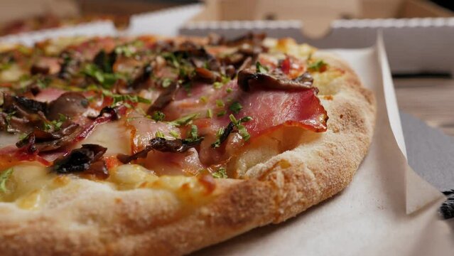 One mushrooms and bacon pizza on black slate platter and wooden table, closeup