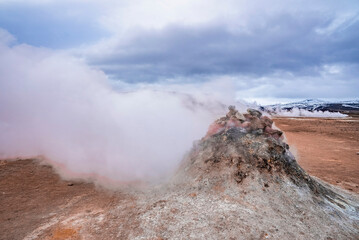Steaming fumarole in geothermal area at Namafjall. Sulphur dioxide erupting from volcanic crater of Hverir. Geyser in famous tourist attraction against cloudy sky.