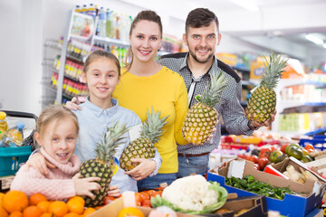 Friendly family of four with fruits and vegetables in greengrocery department of the supermarket