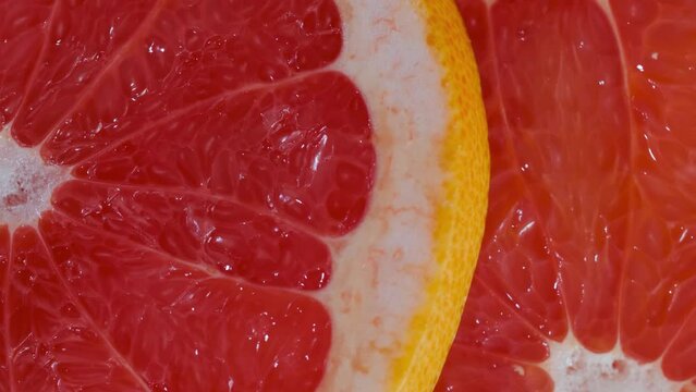 Colorful fresh red citrus fruit slices of grapefruit on rotating surface - macro, close up, top view. Summer, tropical, natural, exotic and healthy food concept