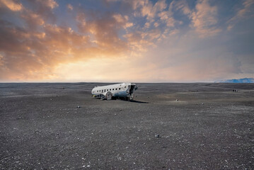 Fototapeta na wymiar View of damaged airplane wreck at black sand beach. Abandoned military aircraft in Solheimasandur against cloudy sky. Scenic view of famous tourist attraction during sunset.