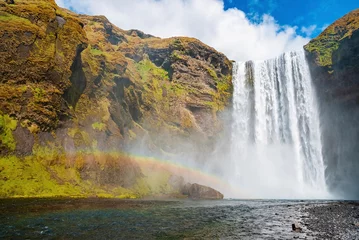Foto op Canvas Low angle view of powerful cascades of Skogafoss waterfall. Beautiful river flowing amidst cliffs in valley. Idyllic natural scenery of volcanic landscape against blue sky. © ingusk