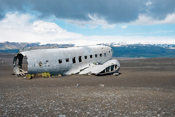Abandoned military aircraft wreck at black sand beach. Broken damaged airplane in Solheimasandur against cloudy sky. View of tourist attraction against mountains.
