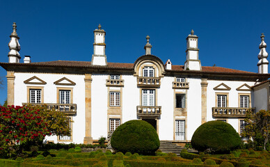 Scenic view of green landscaped backyard and manor building of Mateus Palace with white walls decorated with hewn gray granite, balconies and figured turrets on sunny spring day, Vila Real, Portugal