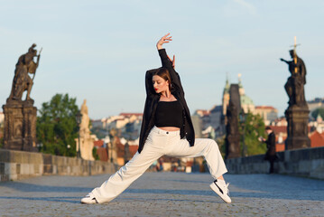 Young woman in casual stylish clothes dancing on the stone bridge of old town in a Prague. Active...