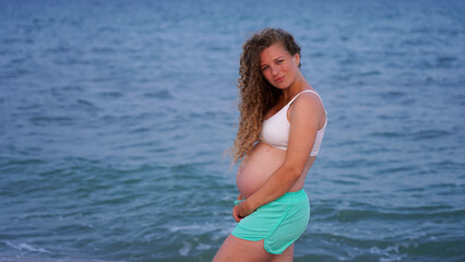 Happy pregnant woman on sea vacation. curly future mother on the background of the sea