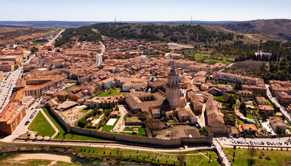 Drone view of Spanish town of El Burgo de Osma in spring overlooking traditional terracotta tiled roofs of residential buildings surrounded by green hills 
