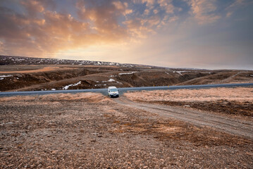 White offroad van moving on road. Scenic view of landscape against cloudy sky in valley. Vehicle used for off-road pathway in northern Alpine region during sunset. © Aerial Film Studio