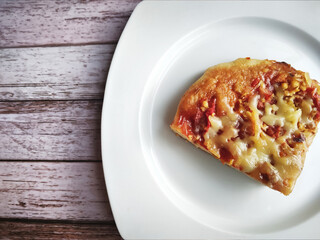 Top view of slice of pizza on a white plate. The pizza is topped with sauce, cheese, tomato, meat and various herbs