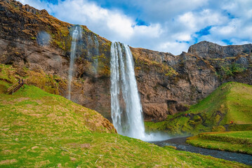 Scenic view of beautiful Seljalandsfoss flowing from mountain. Majestic powerful waterfall against cloudy sky. Picturesque view of famous attraction in valley.