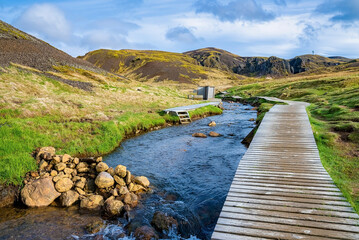 Wooden boardwalk by hot river stream against sky. Scenic view of natural geothermal bath in...