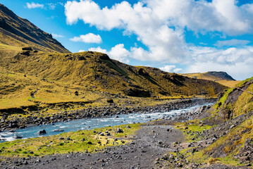 Scenic view of stream flowing amidst landscape. Beautiful green mountain range in valley. Idyllic view of running water against sky in Seljavellir.