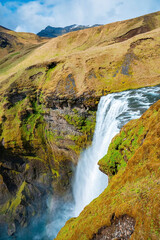 High angle view of powerful cascades of Skogafoss waterfall. Beautiful flowing water amidst cliffs in valley. Scenic natural view of volcanic landscape against cloudy sky.