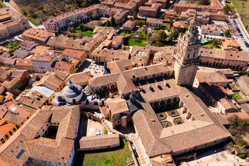 Scenic aerial view of medieval Roman Catholic Cathedral of Assumption of El Burgo de Osma with tall gothic bell tower against brownish tiled roofs of residential buildings on sunny spring day, Spain