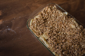 Prepared, unbaked apple crisp sitting on a brown table with flour and crumbs on the table
