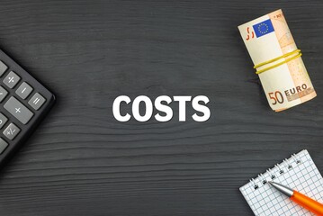 COSTS - word (text) and euro money on a wooden background, calculator, pen and notepad. Business concept (copy space).